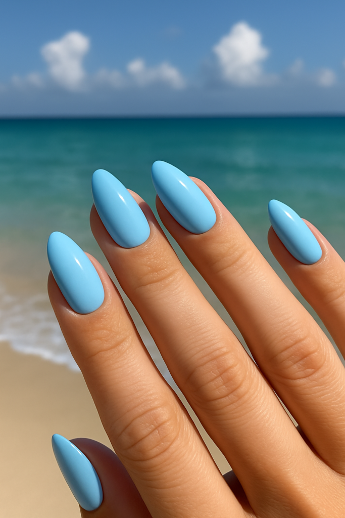 Pastel blue nail polish on almond-shaped nails with beach background